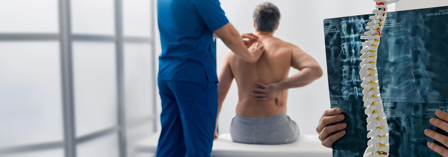 person holding their back while a doctor is feeling the patients spine